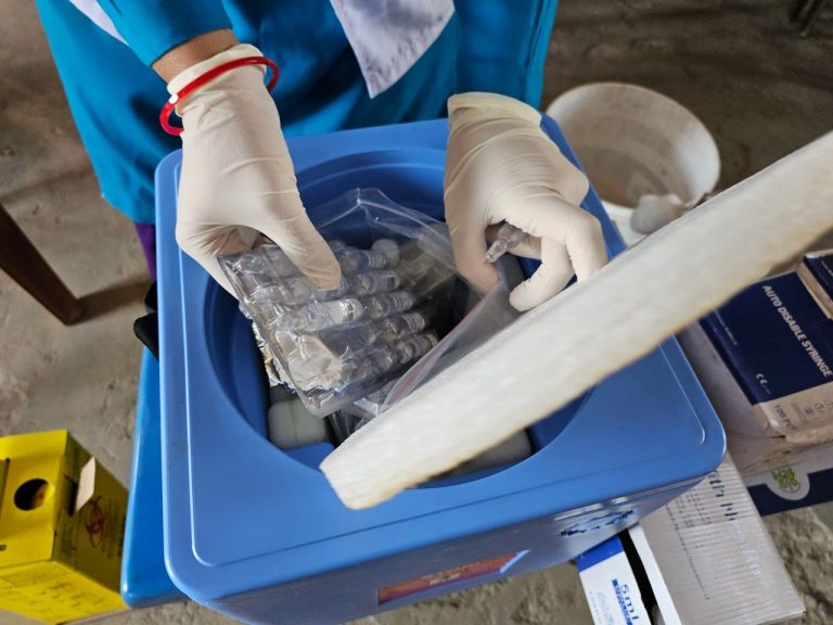 Profissional de saúde usando luvas e manipulando frascos em um laboratório.